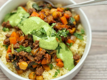 Couscous dish with ground meat, vegetables, and green sauce in a white bowl.
